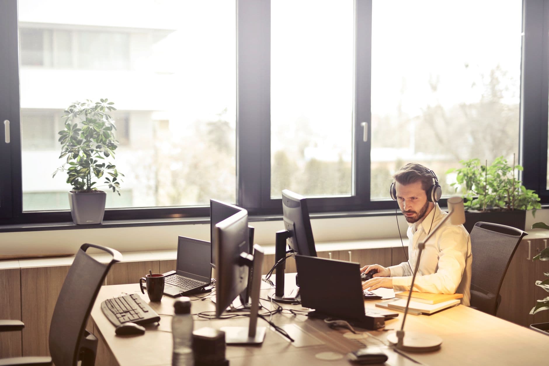 Profesional de TI con auriculares operando varias computadoras en una oficina iluminada