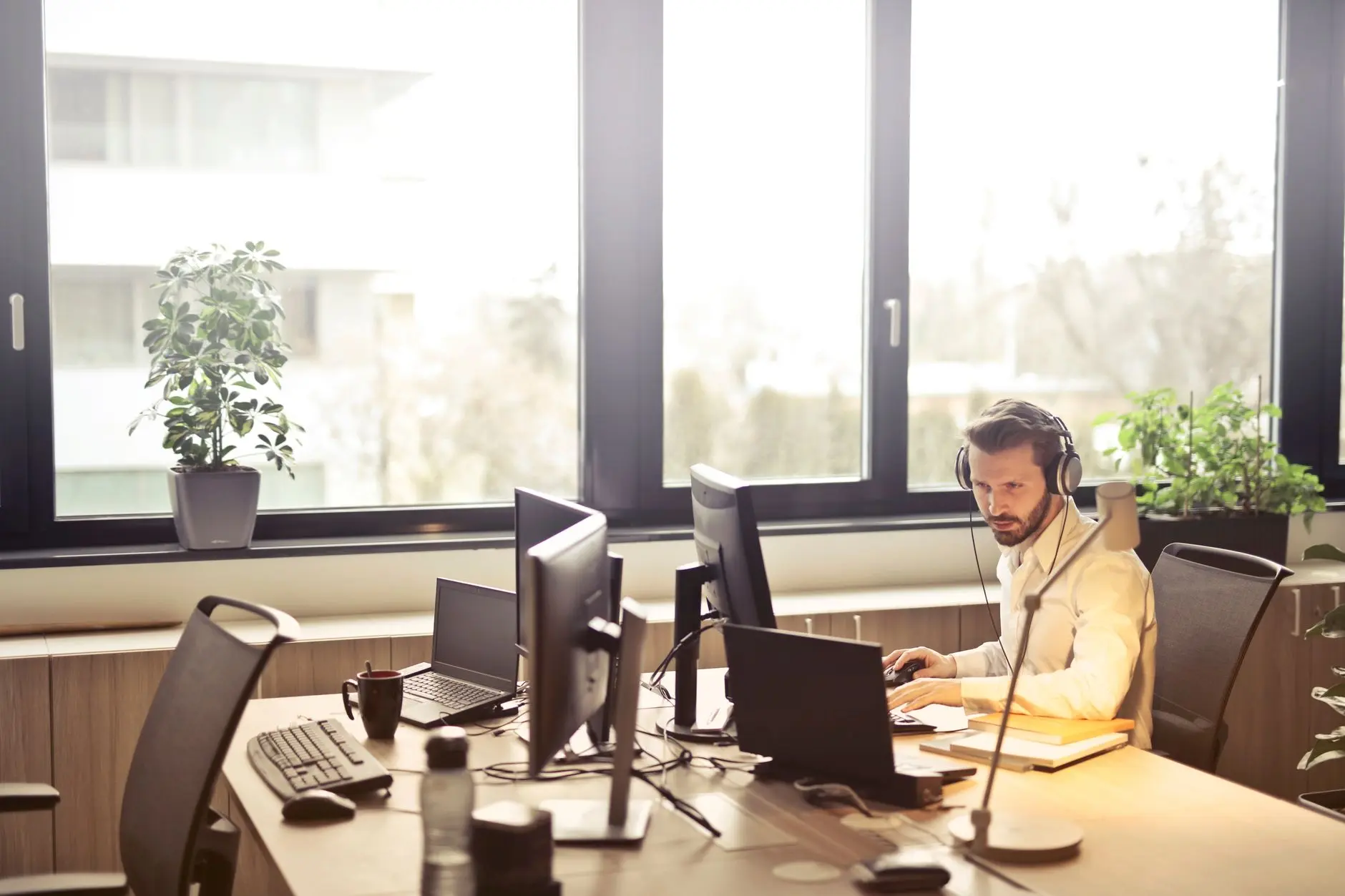 Profissional de TI com headset operando vários computadores em escritório iluminado